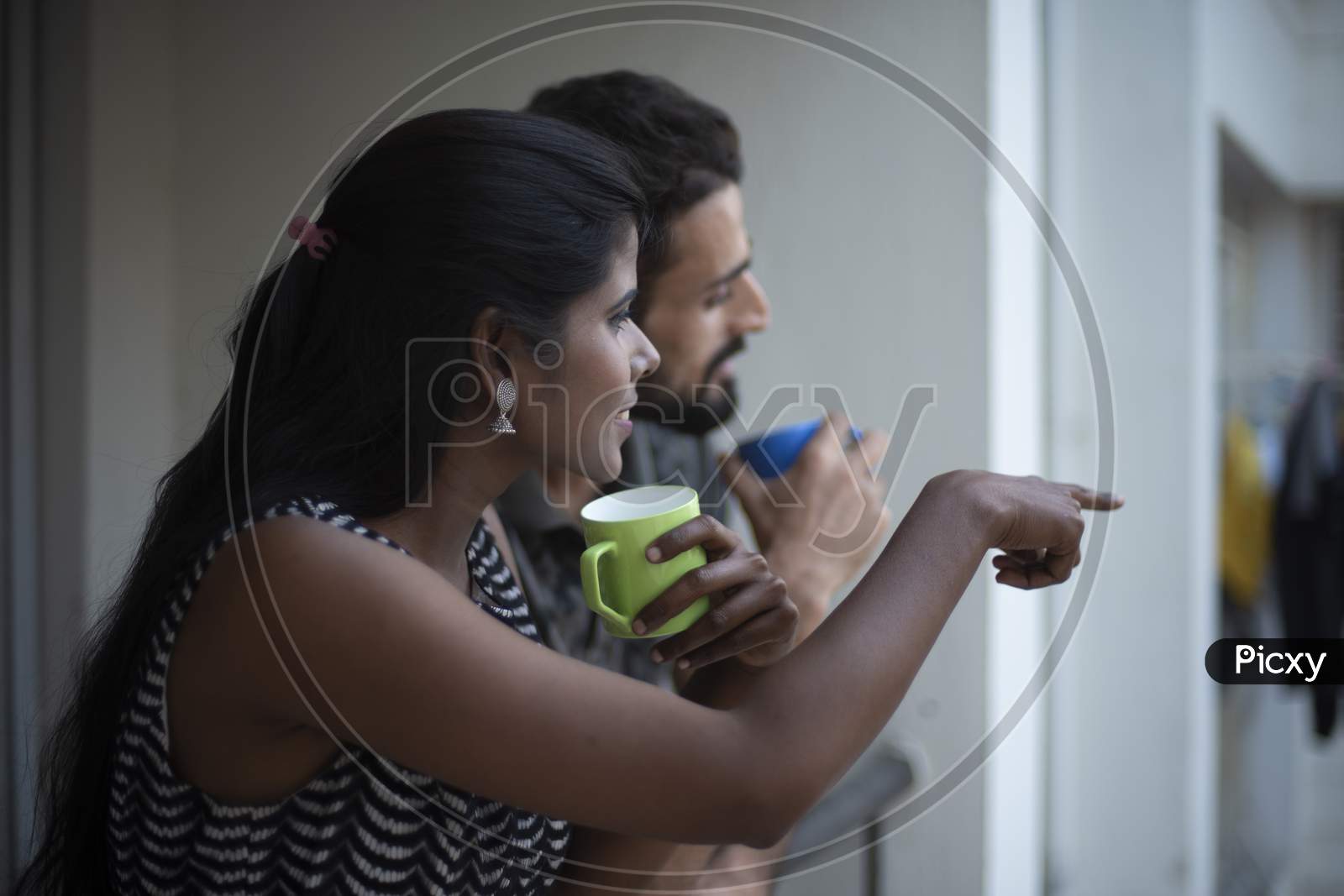 A dark skinned Indian/African girl in  western dress and a Kashmiri/European/Arabian man in casual wear spending time with coffee/tea on a balcony in white background. Indian lifestyle.