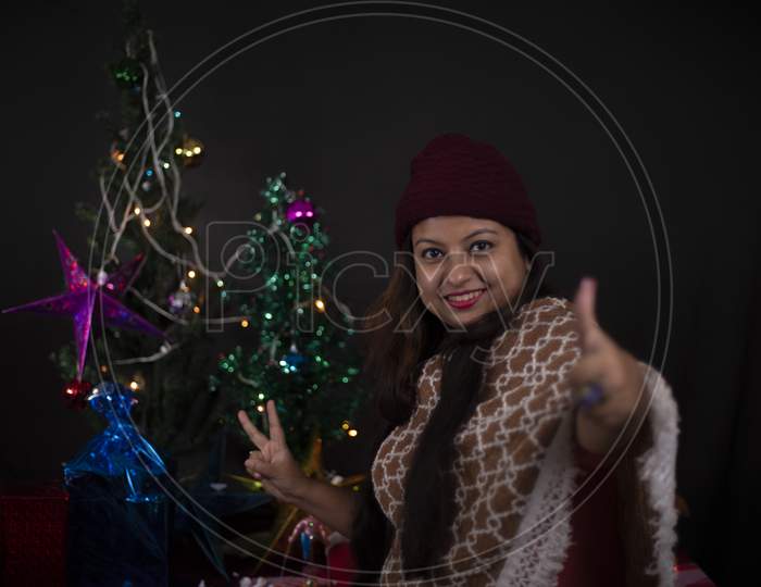portrait of young and cheerful Indian Bengali plus size brunette woman in Santa Clause jacket and hat in decorative Christmas tree background.Indian lifestyle and Christmas celebration