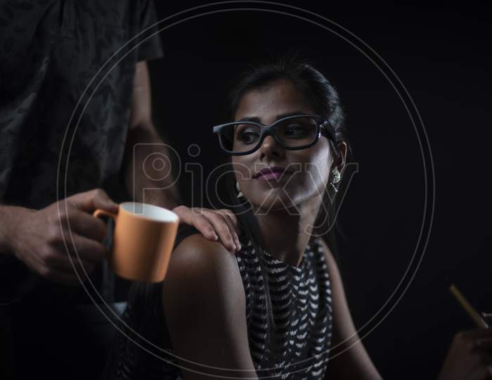 Young brunette Indian/European/Arabian/Kashmiri man offering coffee/tea to his African dark skinned girlfriend/wife in black copy space studio background. Lifestyle of a couple.