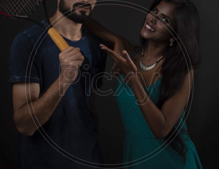 A dark skinned Indian/African girl and a Kashmiri/European/Arabian man in casual wear with tennis racket  in front of a black copy space studio background. Indian lifestyle and fashion photography.