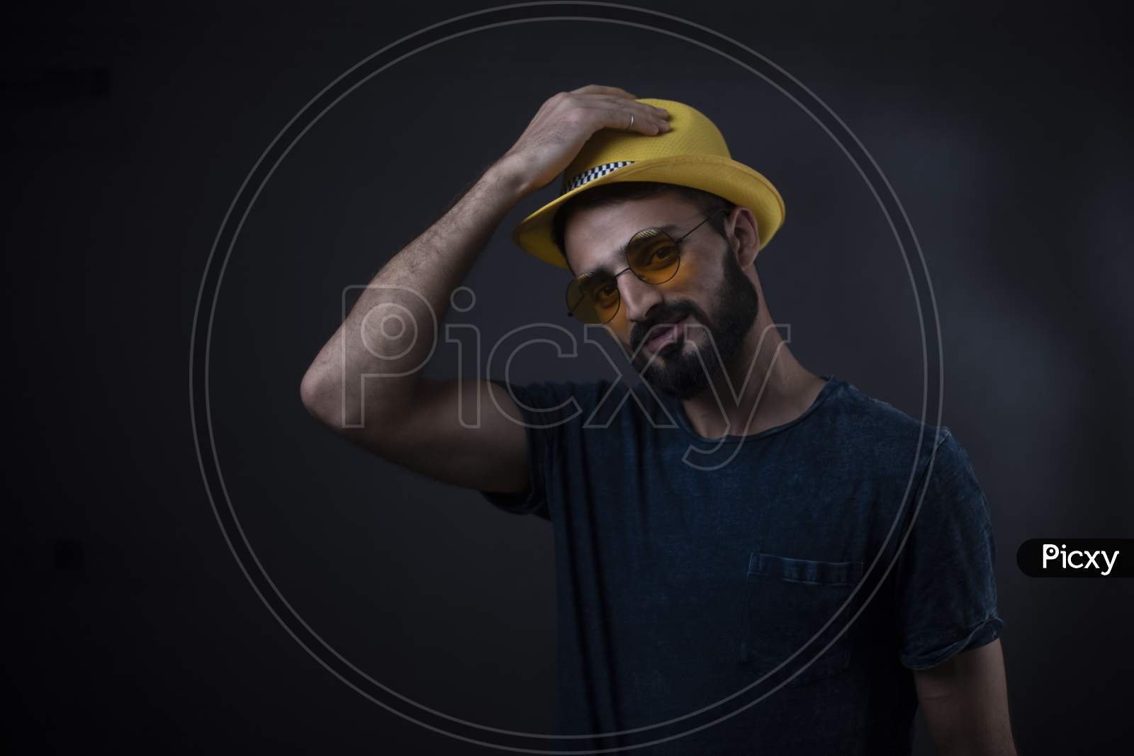 Portrait of young brunette Indian/European/Arabian/Kashmiri man in casual tee shirt with sunglasses and yellow hat in black copy space studio background. lifestyle and fashion.