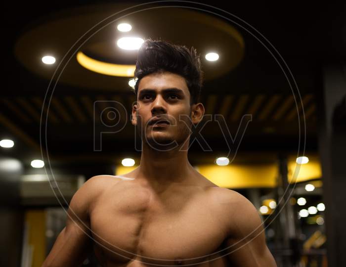 An young and handsome Indian Bengali brunette man with muscular body posing in a multi gym. Fitness and Indian lifestyle.