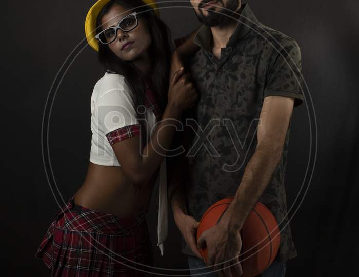 A dark skinned Indian/African girl in school uniform and hat and a Kashmiri/European/Arabian man in casual wear with basket ball in front of black copy space studio background. Indian lifestyle.