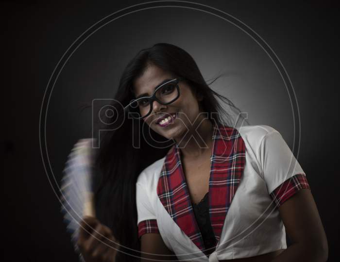 Portrait of an Asian/Indian/African brunette dark skinned young girl in fashionable trendy school uniform and spectacles with Chinese fan in a black/grey studio background. Fashion and cosplay photography.