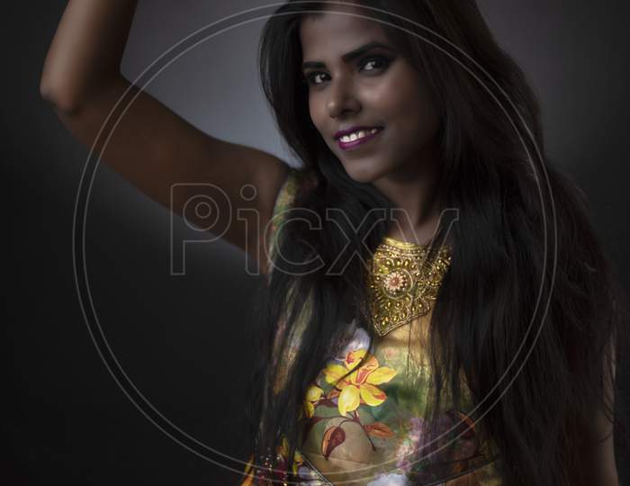 Fashion portrait of young dark skinned Indian Bengali brunette girl in floral dress with yellow hat in front of black copy space studio background. Indian fashion portrait and lifestyle.