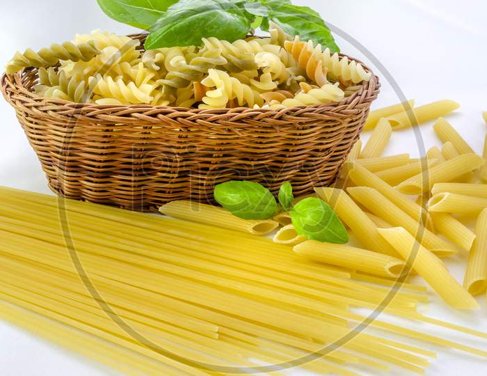 Uncooked mixed pasta with a basket on a white background.