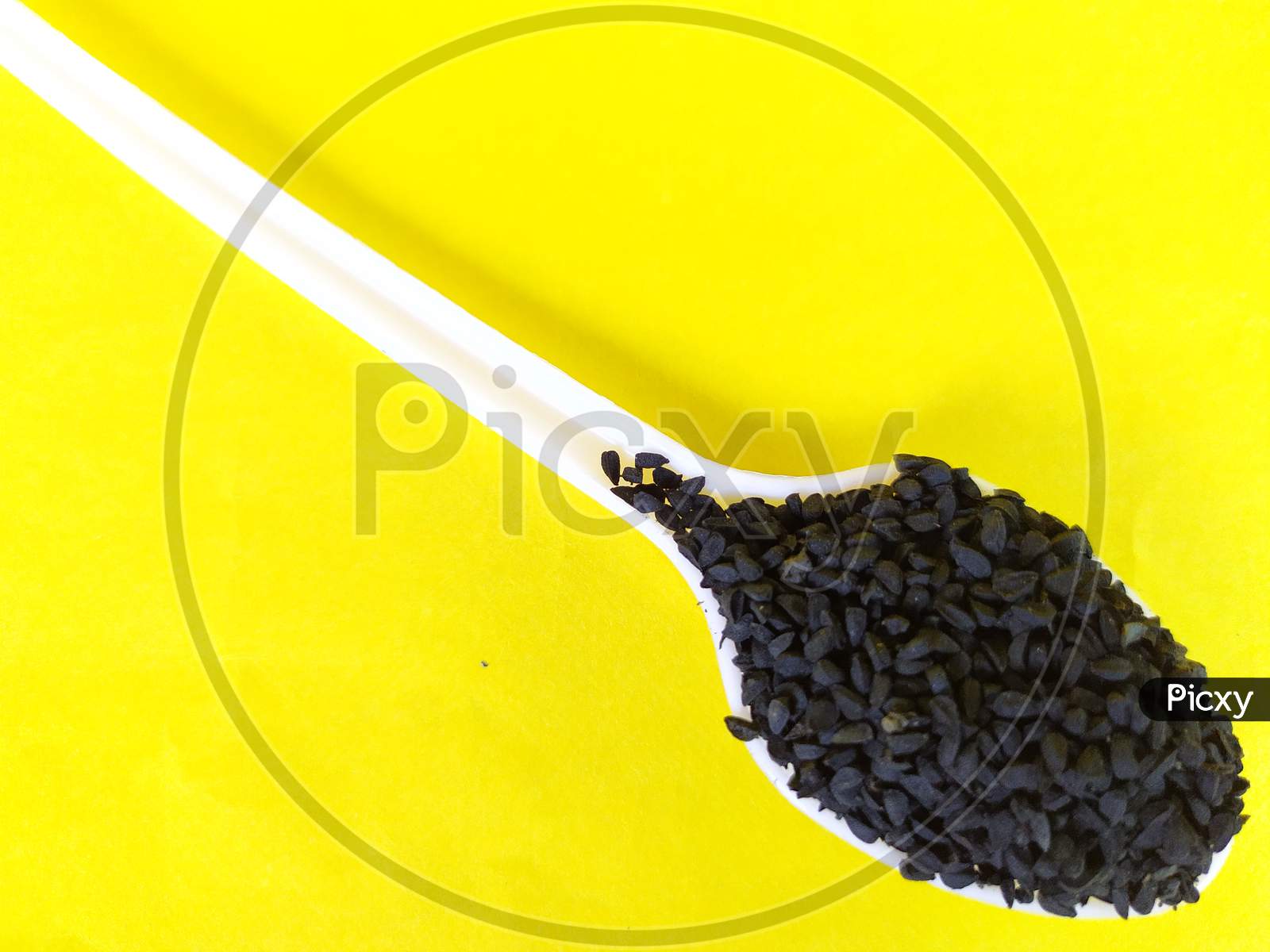 Black cumin seeds in a spoon, Yellow background.