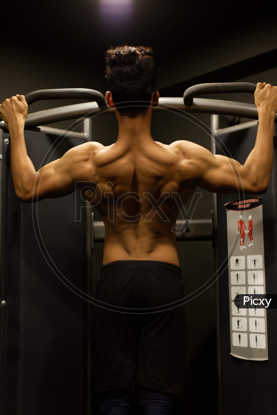 An young and handsome Indian Bengali brunette man with muscular body showing his muscular backside while exercising in a multi gym. Fitness and Indian lifestyle.
