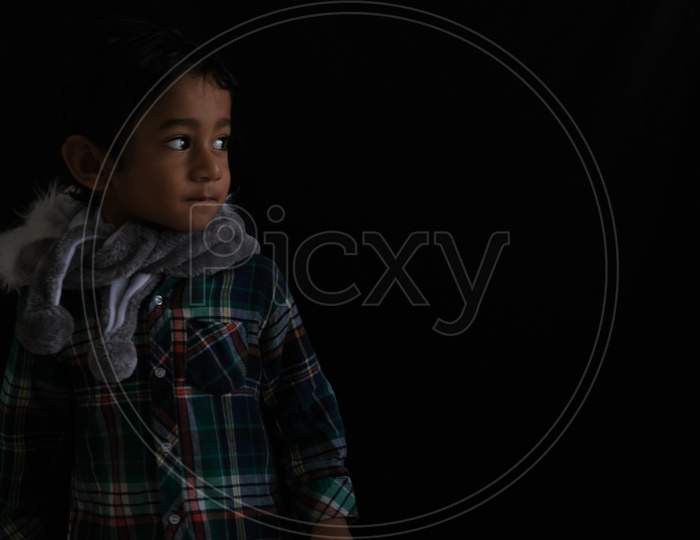 Portrait of Indian cute little cheerful brunette Tamil baby boy wearing casual dress with a furry toy in a black background. Indian lifestyle.
