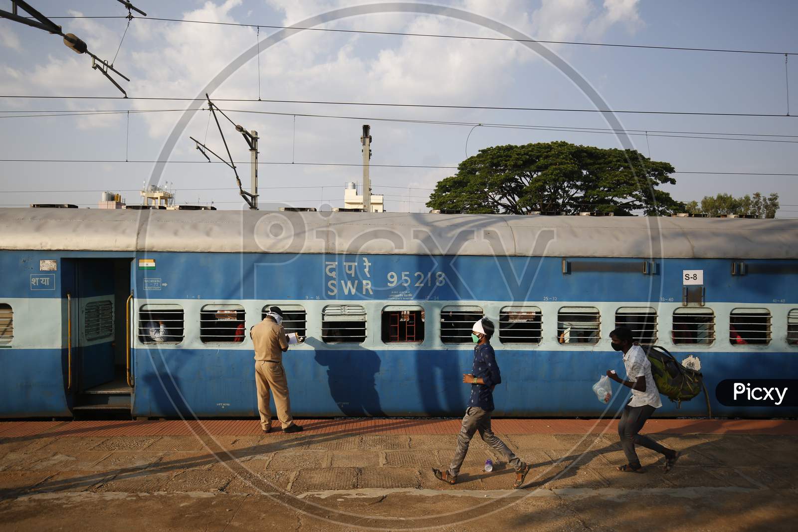 Men run past a Railway Protection Force (RPF) personnel as he checks travel documents of people travelling to Danapur, Bihar in a special train arranged by the government to repatriate migrant workers at the Chikkabanavara Junction Railway Station on the outskirts of Bangalore, India.