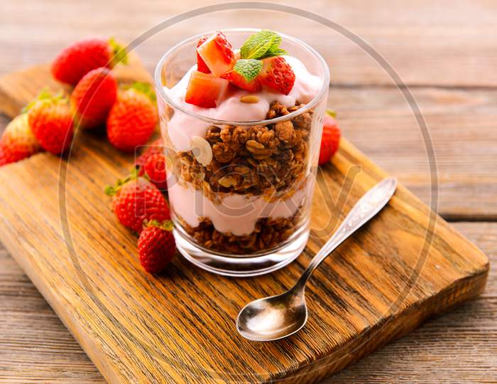 Healthy layered dessert with muesli and berries on a wooden plate