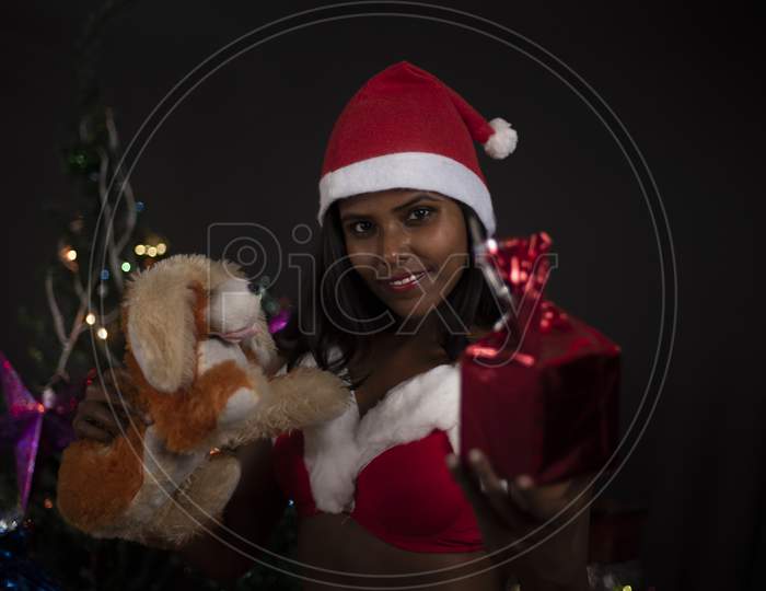 Portrait of young Indian Bengali dark skinned brunette woman in Santa Clause lingerie, jacket and hat with gifts in decorative Christmas tree background.Indian lifestyle and Christmas celebration.
