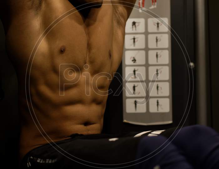 Abdominal muscles of an young and handsome Indian Bengali brunette man with muscular body doing exercise in a multi gym. Fitness and Indian lifestyle.