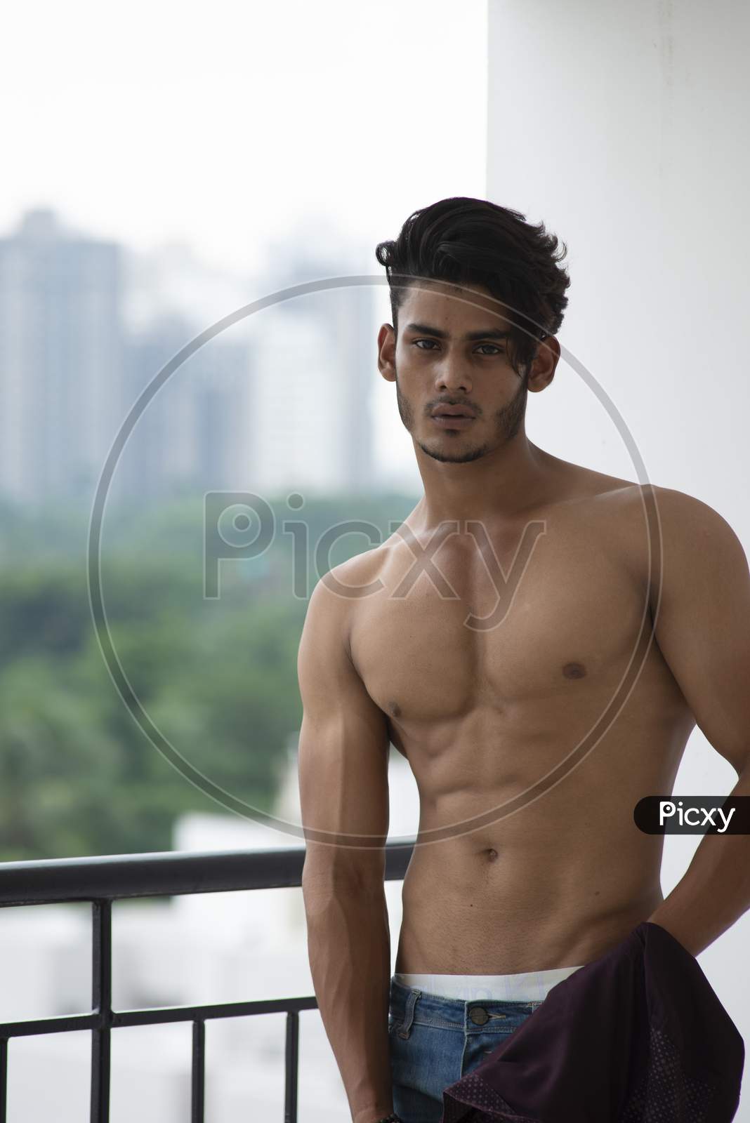 Image of Portrait of an young and handsome brunette Bengali muscular man in  bare body standing on a balcony in urban background. Indian  lifestyle.-YC151508-Picxy