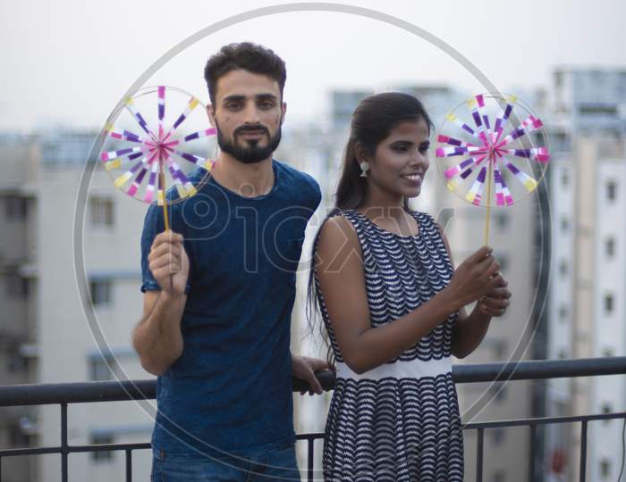 A dark skinned Indian/African girl in  western dress and a Kashmiri/European/Arabian man in casual wear playing with pinwheel on a rooftop in urban background. Indian lifestyle.