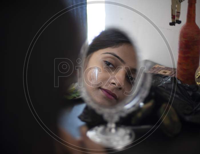 Reflection of the face of an young and attractive Indian brunette woman with a patch of white beauty cream on her face. Indian lifestyle