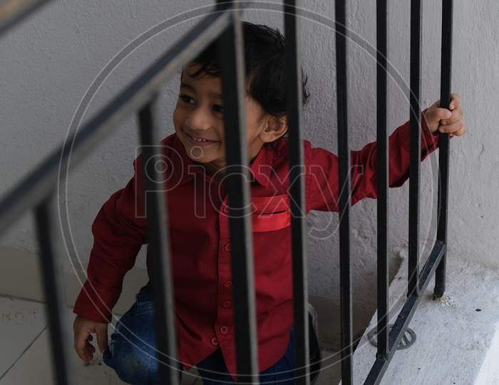 Portrait of Indian cute little cheerful brunette Tamil baby boy wearing vibrant red shirt while standing on a balcony in a white background. Indian lifestyle.