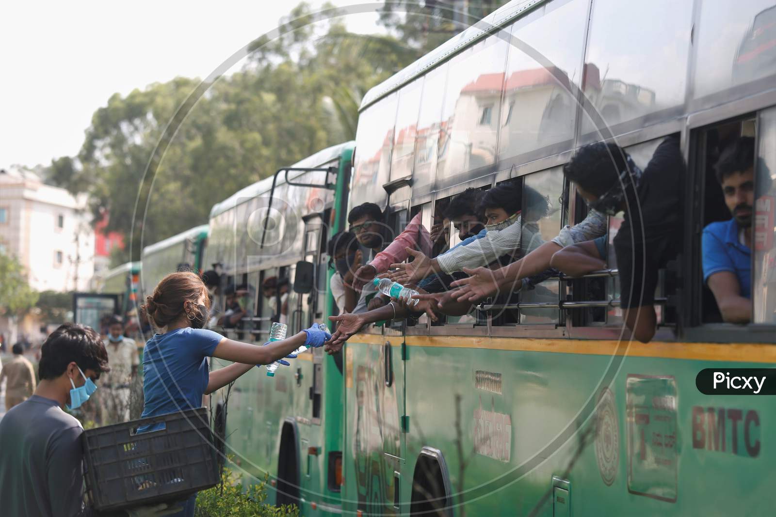 A woman provides bottles of drinking water to men inside a bus as they wait to alight to board a special train arranged by the government to repatriate migrant workers from the Chikkabanavara Junction Railway Station on the outskirts of Bangalore, India.