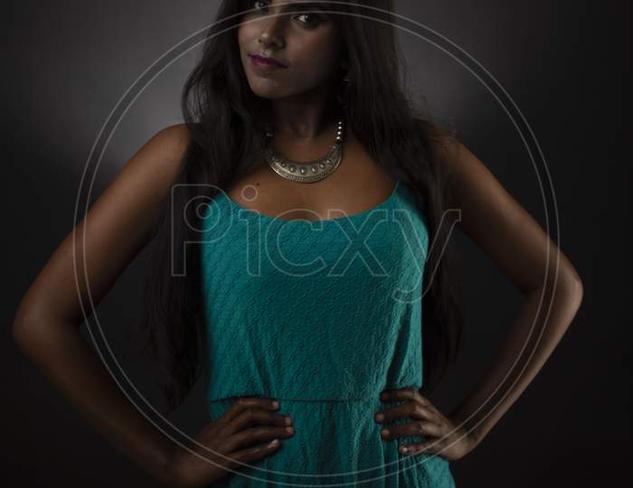 Fashion portrait of young dark skinned Indian/African brunette girl in green western dress and jewelry in front of black copy space studio background. Indian fashion photography.
