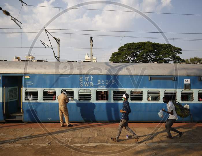 Men run past a Railway Protection Force (RPF) personnel as he checks travel documents of people travelling to Danapur, Bihar in a special train arranged by the government to repatriate migrant workers at the Chikkabanavara Junction Railway Station on the outskirts of Bangalore, India.