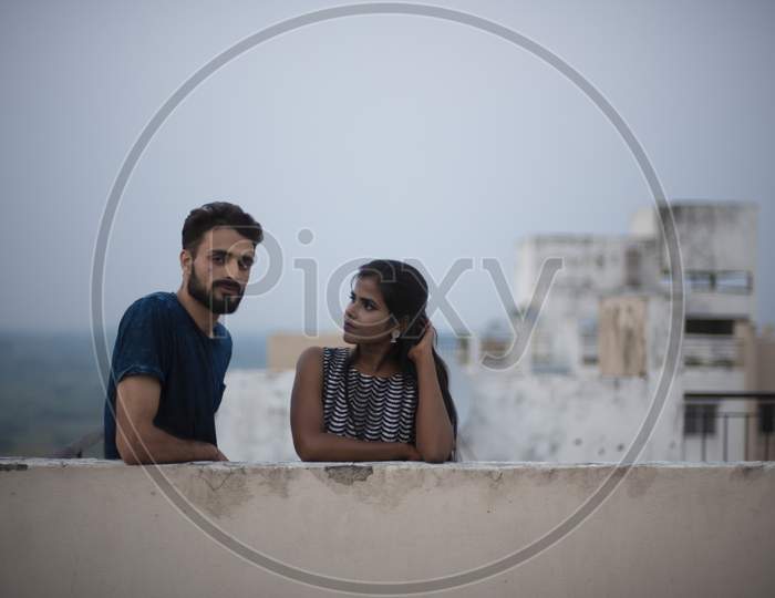 A dark skinned Indian/African girl in  western dress and a Kashmiri/European/Arabian man in casual wear spending time on a rooftop in the afternoon in urban background. Lifestyle of a couple.
