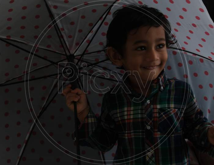 Portrait of Indian cute little cheerful brunette Tamil baby boy wearing casual dress with an umbrella in a black background. Indian lifestyle.