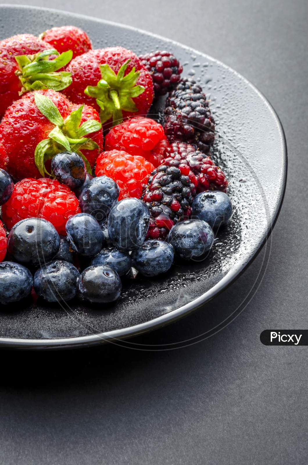 A vertical shot of a plate of fresh summer fruit on a dark background.