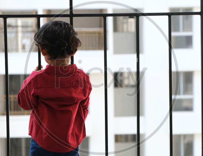 Backside portrait of Indian cute little cheerful brunette Tamil baby boy wearing vibrant red shirt while standing on a balcony in a white urban background. Indian lifestyle.