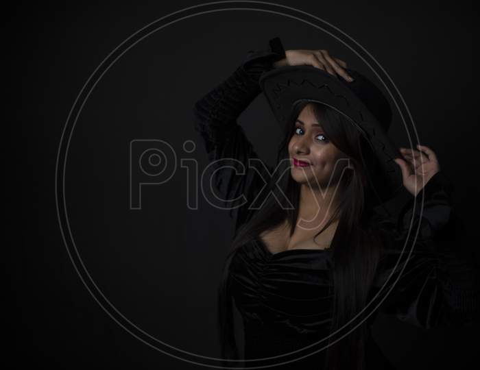 Fashion portrait of an young and attractive Indian Bengali brunette girl with black western dress with a cowboy hat in front of a black studio background. Indian fashion portrait and lifestyle.