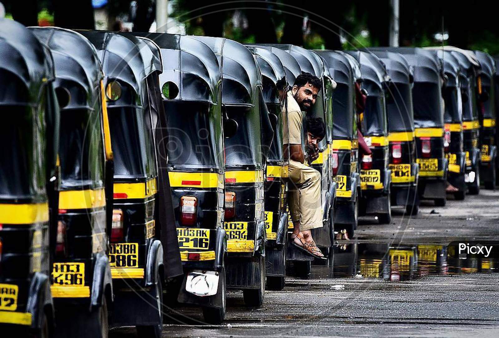 Auto rickshaws in line are parked parallel to one another