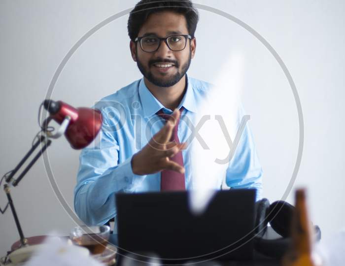 Indian Bengali tall, dark, handsome brunette young man in office wear enjoying success while sitting on an office table  in a corporate office/bpo/call center. Indian corporate lifestyle.
