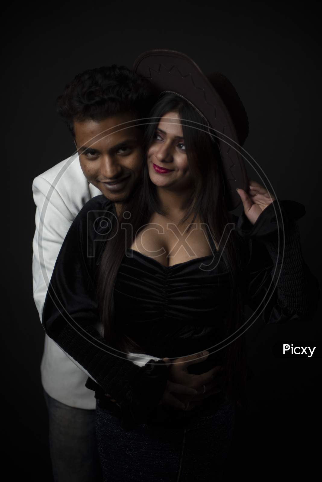 Close up portrait of an young and attractive Indian brunette Bengali couple with western dresses and cowboy hat in black studio copy space background. Indian fashion portrait and lifestyle