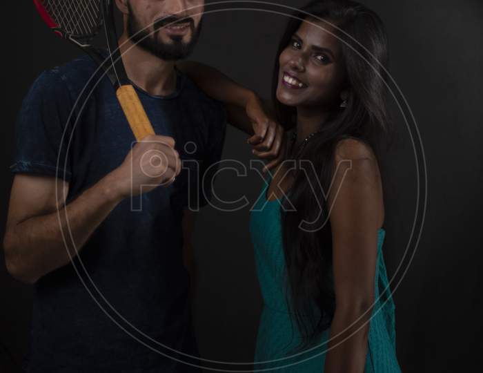 A dark skinned Indian/African girl and a Kashmiri/European/Arabian man in casual wear with tennis racket  in front of a black copy space studio background. Indian lifestyle and fashion photography.