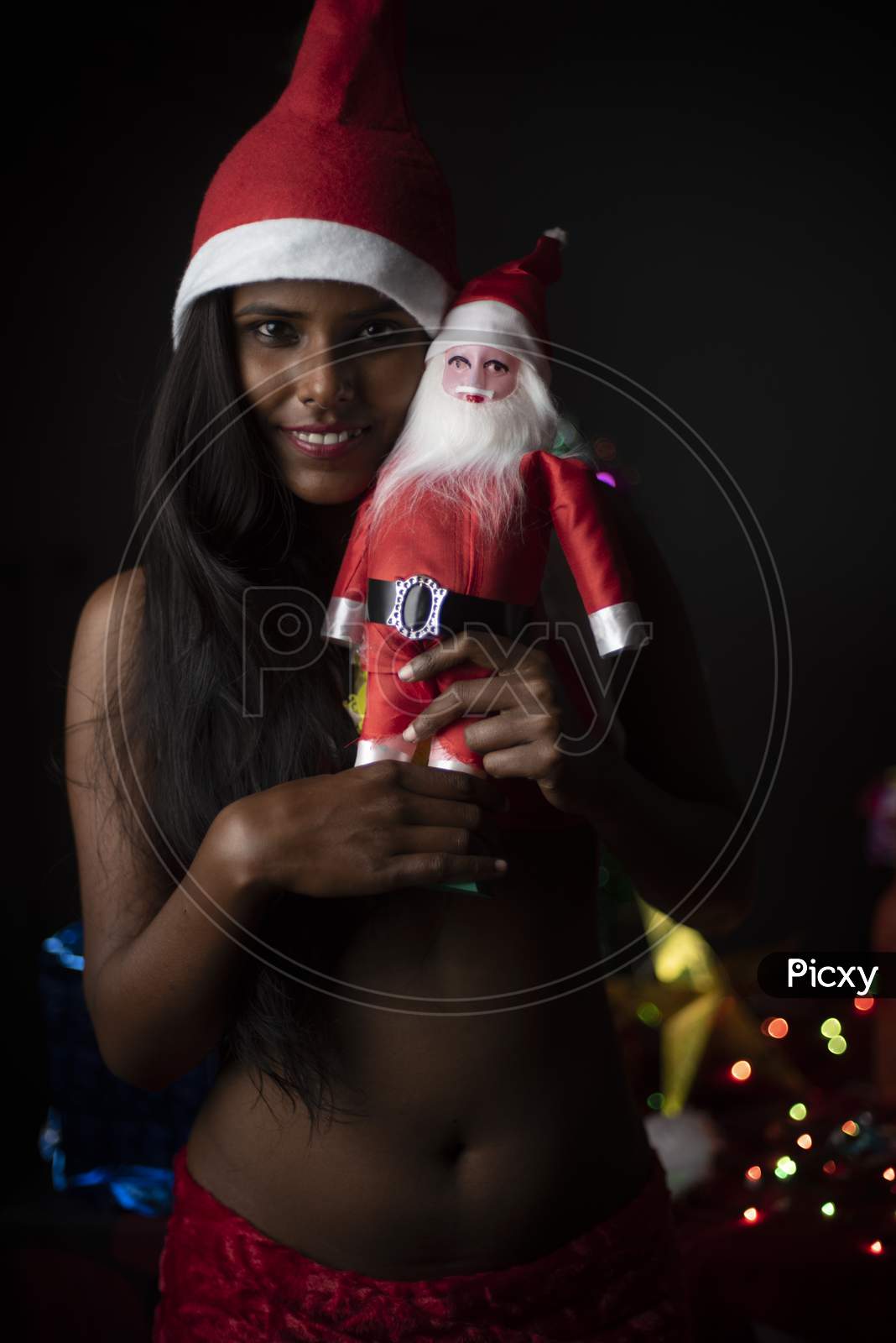 Portrait of young Indian Bengali dark skinned brunette woman in Santa Clause lingerie, gifts and soft toys in decorative Christmas tree background.Indian lifestyle and Christmas celebration.