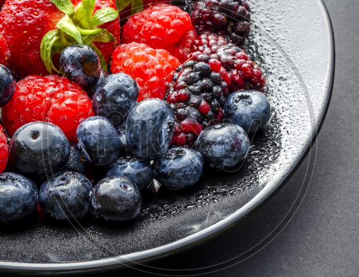 A vertical shot of a plate of fresh summer fruit on a dark background.