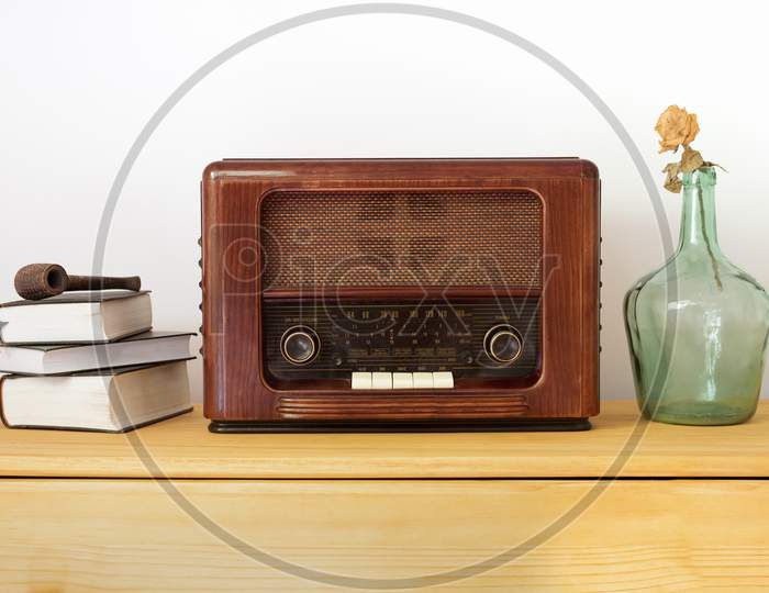Vintage radio made of wood, old books, green vase and a pipe on a table