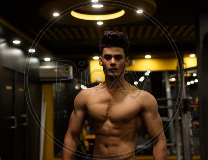 An young and handsome Indian Bengali brunette man with muscular body posing in a multi gym. Fitness and Indian lifestyle.
