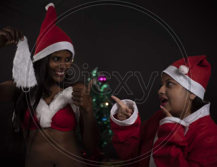 Young Indian Bengali woman wearing Santa Clause lingerie and plus size woman in Santa Clause costume enjoying in decorative Christmas tree background.Indian lifestyle and Christmas celebration.