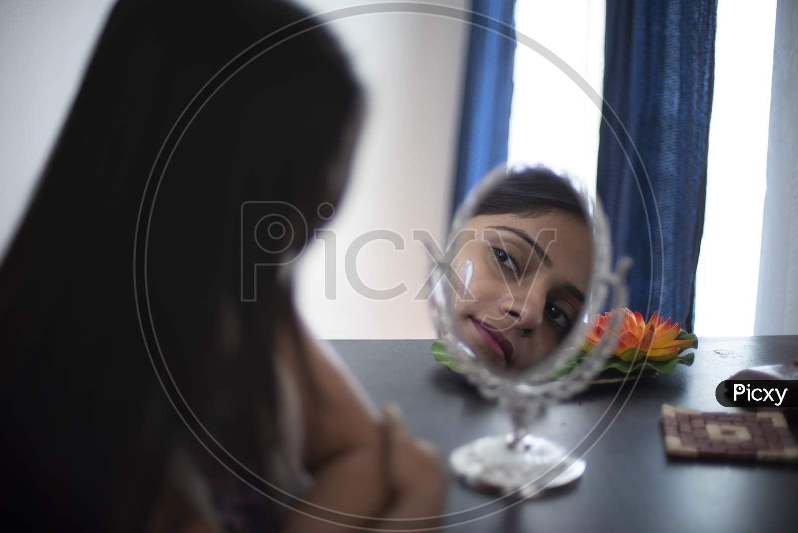 Reflection of the face of an young and attractive Indian brunette woman with a patch of white beauty cream on her face. Indian lifestyle