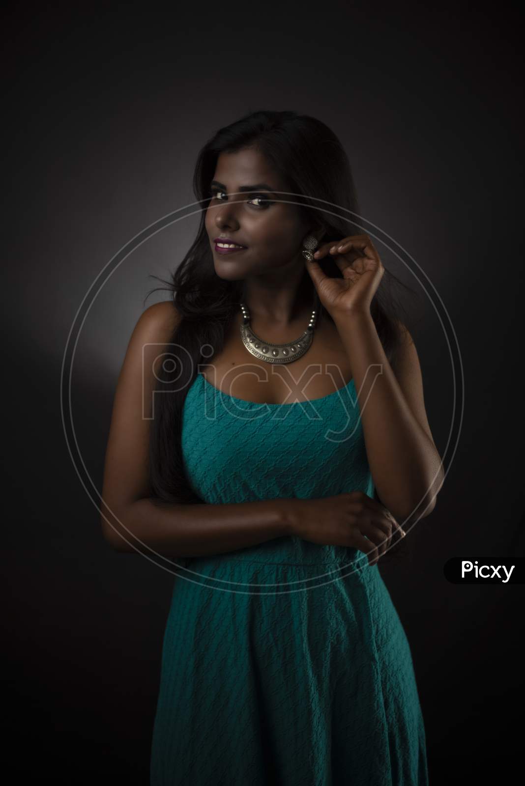 Fashion portrait of young dark skinned Indian/African brunette girl in green western dress and jewelry in front of black copy space studio background. Indian fashion photography.
