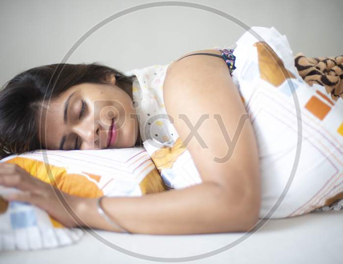 Top down portrait of an young and attractive Indian Bengali brunette woman in white sleeping wear is lying on a white bed with white cushions and blanket in her bedroom. Indian lifestyle.