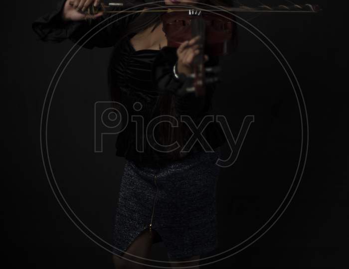 Fashion portrait of an young and attractive Indian Bengali brunette girl with black velvet dress is playing violin in front of a black studio background. Indian fashion portrait and lifestyle.