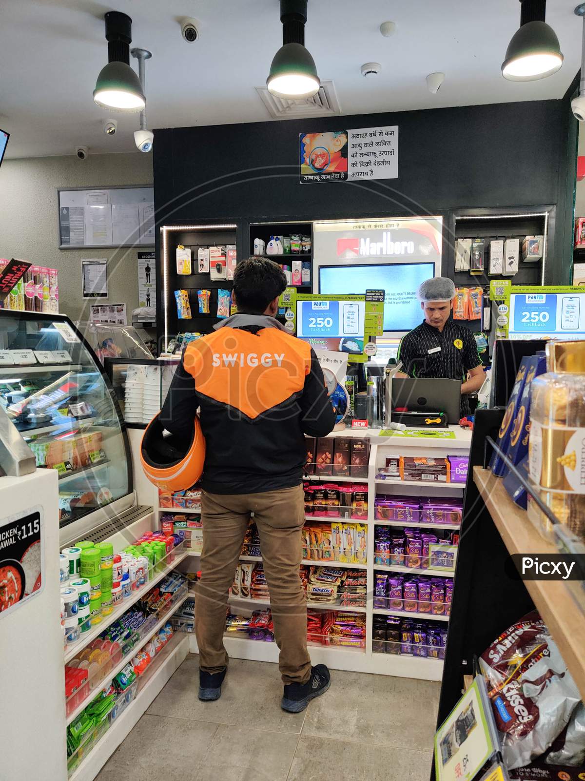 Swiggy Store Delivery Agent Standing At The Counter Of A Departmental Store Collecting An Order For Home Delivery