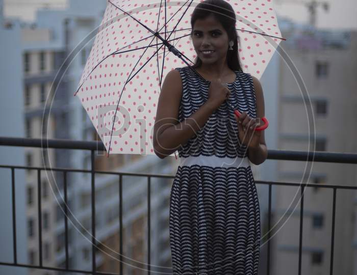 Portrait of a young dark skinned Indian/African girl in western dress standing with umbrella on a rooftop in the afternoon in urban background. Indian lifestyle.