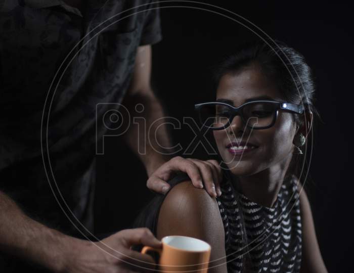 Young brunette Indian/European/Arabian/Kashmiri man offering coffee/tea to his African dark skinned girlfriend/wife in black copy space studio background. Lifestyle of a couple.