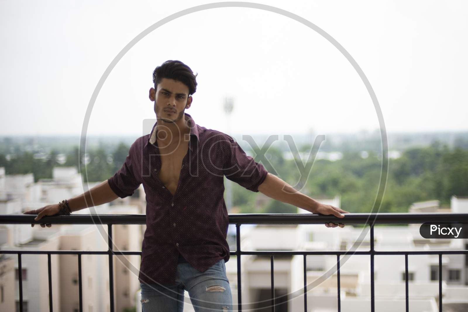 Image of Portrait of an young and handsome brunette Bengali muscular man in  casual shirt and jeans standing on a balcony in white urban background.  Indian lifestyle.-LC597067-Picxy