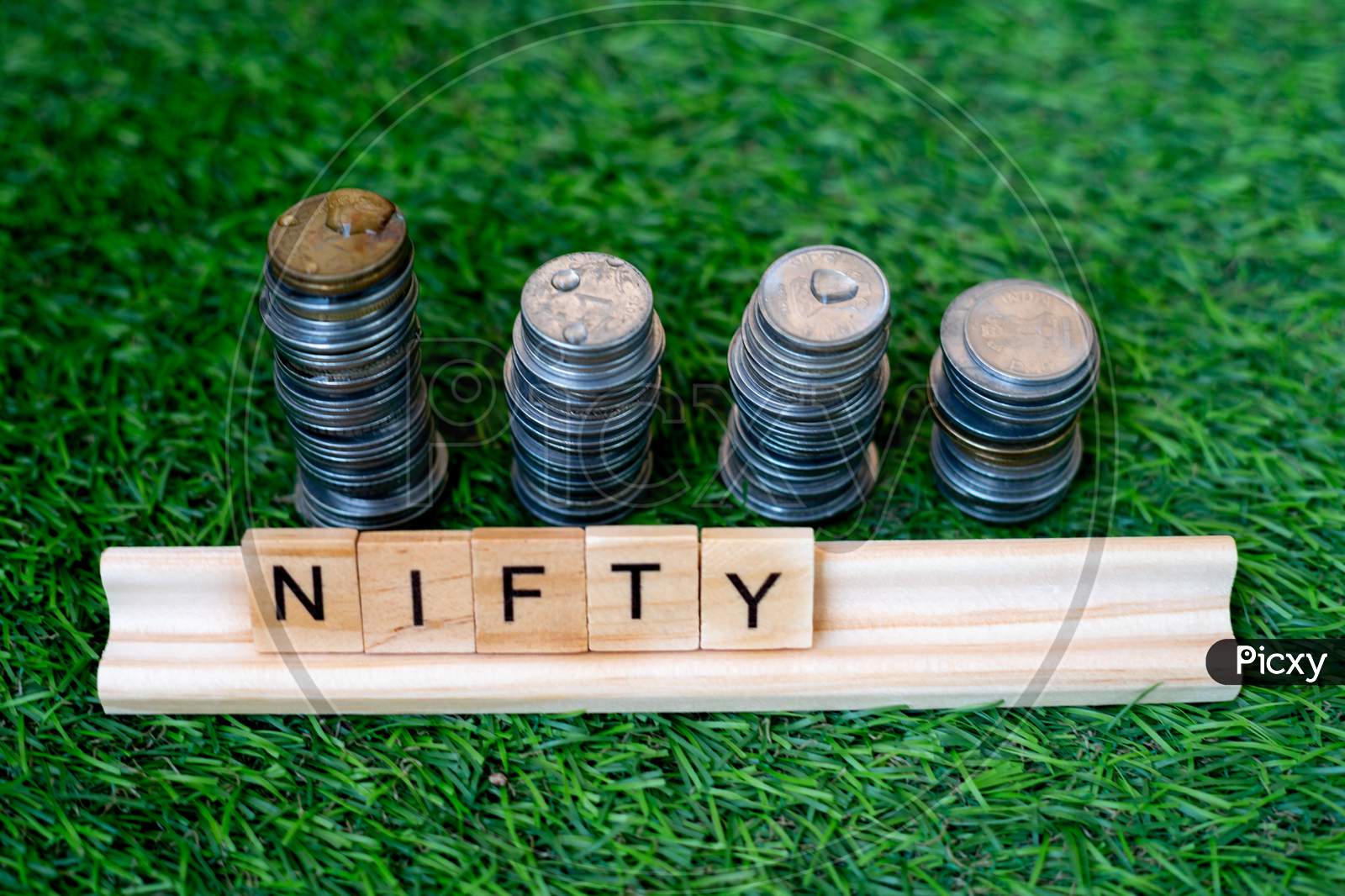 Wooden Blocks With Nifty Written On Them With A Growing Stack Of Coins Behind It Sitting On Grass