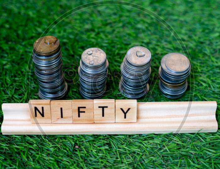 Wooden Blocks With Nifty Written On Them With A Growing Stack Of Coins Behind It Sitting On Grass