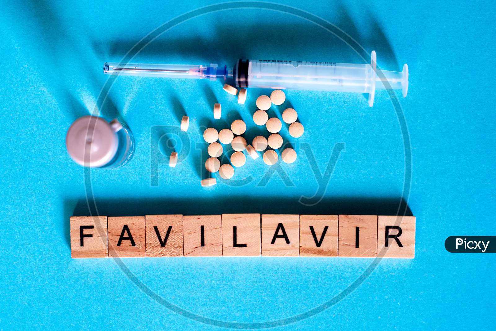 Shot Of Tablets, Glass Bottle, Syringe On Blue And Wooden Blocks With Favilavir The Antiviral Drug Used For Covid19 Coronavirus Written On It. Shows One Of The Key Drugs Being Tested To Cure Coronavirus Patients