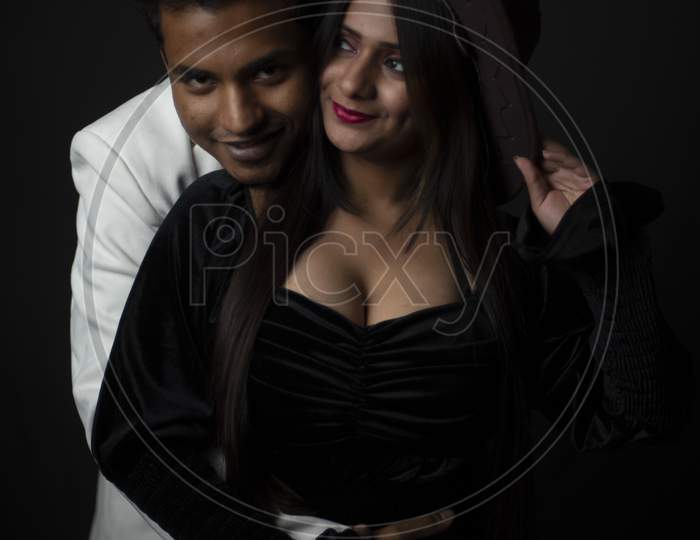 Close up portrait of an young and attractive Indian brunette Bengali couple with western dresses and cowboy hat in black studio copy space background. Indian fashion portrait and lifestyle